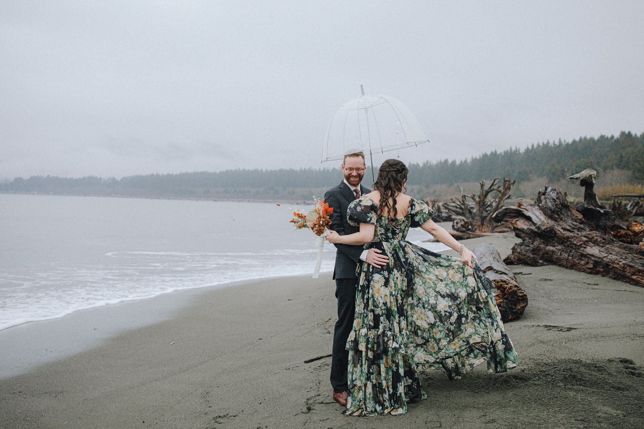 Vancouver Island wedding photo featuring a couple on the beach under an umbrella in rainy weather.